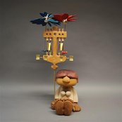 Pyramidenengel sitzende Figur hält ein Gebilde mit Blumen an einem Stab hoch